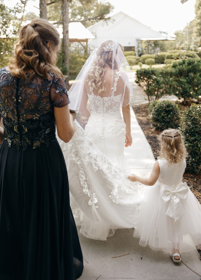 Bride walking towards wedding ceremony with little girl holding her dress